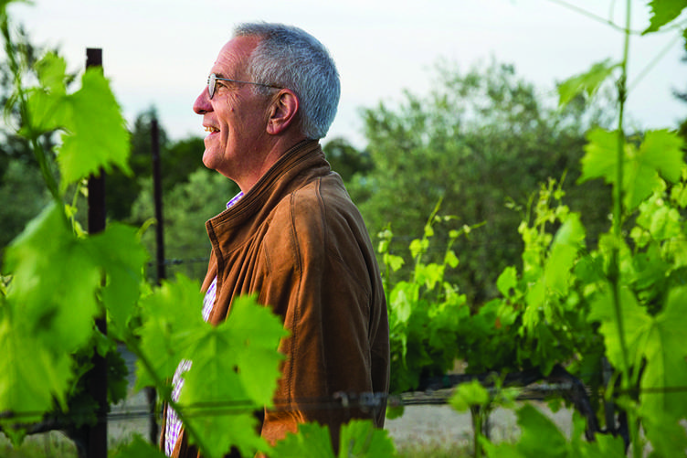 Ridgely Evers standing smiling in his vineyard looking off into the distance