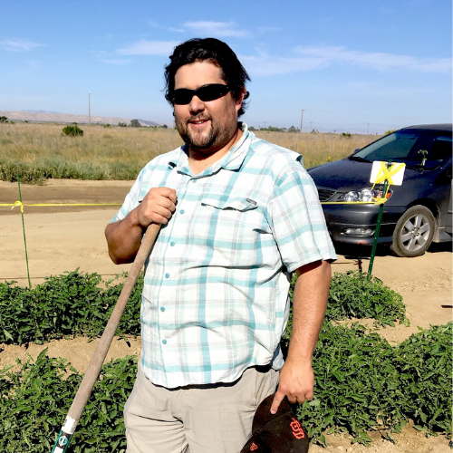 Rod Kumimoto standing in a field with a shovel in his hands.